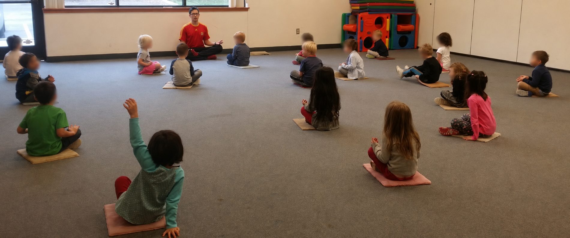 A group of preschoolers sitting cross-legged on mats in a mindfulness session led by Coach Matt